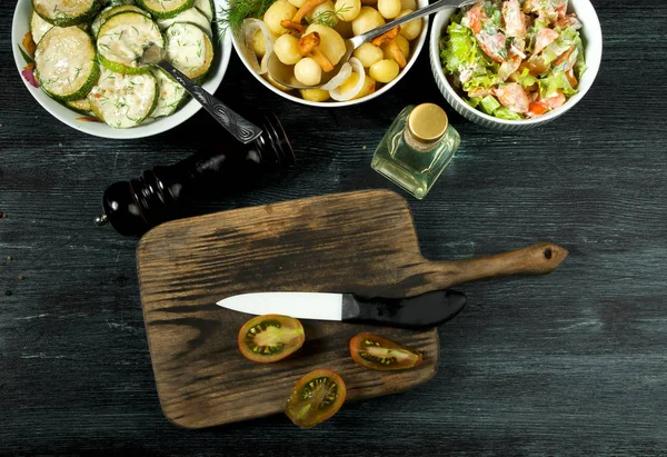 Verduras en el fondo. Salsa de calabacín frito en un plato. Patatas jóvenes hervidas con eneldo en un tazón. Las setas fritas de la cantarela con la cebolla dorada en la sartén. espacio de copia — Foto de Stock