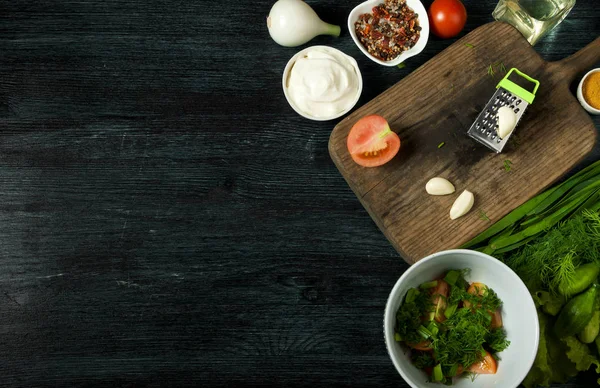 Ensalada con verduras. Vista desde arriba. Ensalada fresca en un plato sobre un fondo oscuro. Ajo, tomate, pepino, eneldo y cebolla en un plato de superficie oscura. Copiar espacio . Imagen De Stock