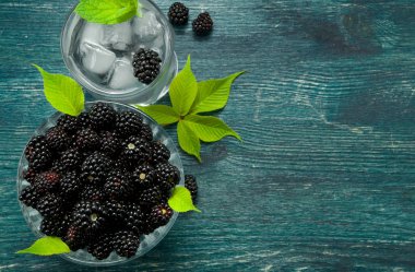 Taze böğürtlen. Bir kase sulu böğürtlen ve ahşap bir masada çilek ile soğuk buzlu su bir bardak. Yukarıdan görüntüleyin. Kopyalama alanı.