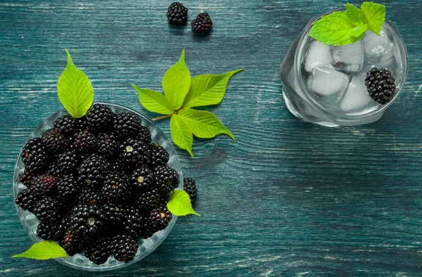 Fresh blackberry. Juicy blackberry in a bowl and a glass of cold ice water with berries on a wooden table. View from above. Copy space. — Stock Photo, Image