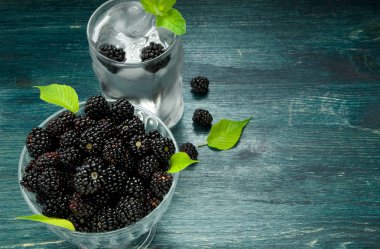 Taze böğürtlen. Bir kase sulu böğürtlen ve ahşap bir masada çilek ile soğuk buzlu su bir bardak. Yukarıdan görüntüleyin. Kopyalama alanı.