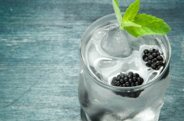 Tatlı su. Yaban mersini, buz küpleri ve ahşap bir masada nane ile bir bardak serin tatlı su. Yukarıdan görüntüleyin. Kopyalama alanı.