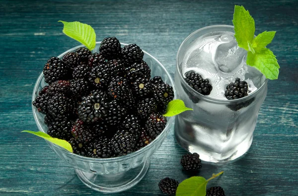 Fresh blackberry. Juicy blackberry in a bowl and a glass of cold ice water with berries on a wooden table. View from above. Copy space.