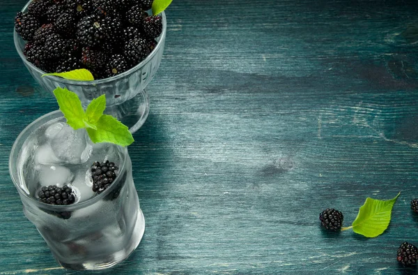 Taze böğürtlen. Bir kase sulu böğürtlen ve ahşap bir masada çilek ile soğuk buzlu su bir bardak. Yukarıdan görüntüleyin. Kopyalama alanı.