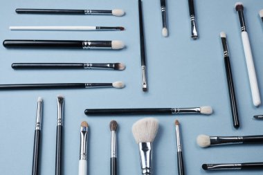 Farklı boyutlarda beyaz ve siyah renkte makyaj veya çizim için fırçalar mavi arkaplanda farklı yönlere yatar.