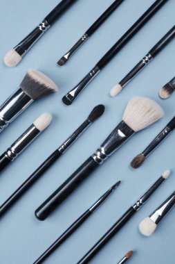 Farklı boyutlarda beyaz ve siyah renkte makyaj veya çizim için fırçalar mavi arkaplanda farklı yönlere yatar.