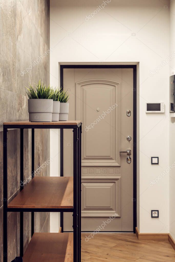 Textured wall with concrete tiles in the lobby. Front door, hanger and rack in one modern style. Concrete ceiling, wall and straight light at the entrance to the room with plants