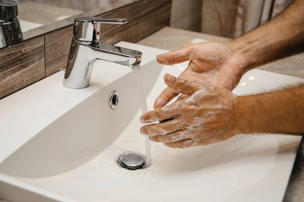 Human is washing hands with soap for corona virus prevention. Water flows from the water mixer and a man lathers his hands for stopping the spread of infection coronavirus