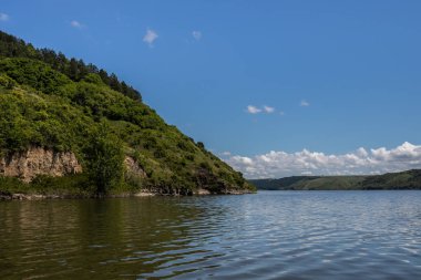 Dinyester'in yüksek ve dik kıyısı, yeşil otlar, çalılar ve ormanlarla kaplıdır. Ufukta gökyüzünü ve bulutları temizleyin. Yaz manzarası. Ukrayna.