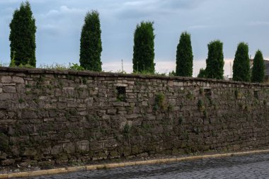 Eski, çim çalıları ile kaplı, taş duvar ve karanlık bir gökyüzü arka planda arkasında yeşil ağaçlar bir dizi.