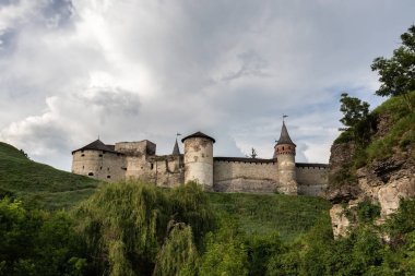 Bulutlu gökyüzünde ön planda yeşillik ve kayaların arka planına karşı Xvi yüzyılın ortaçağ Kamianets-Podilskyi kale parçası. Ukrayna.