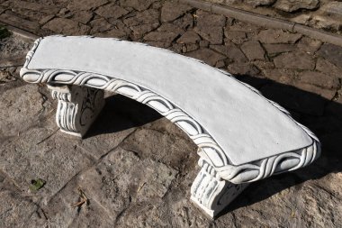 Parktaki taş kaldırımın arka planında beyaz oyma küçük bank.