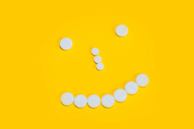 sarı bir arka plan üzerinde hap lar ve vitaminler ile ortaya konan bir gülümseme ile yüz. yukarıdan görünüm