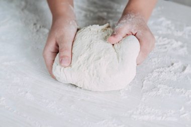 Beyaz ahşap masa arka plan üzerinde kadın eller ile hamur yapma. Beyaz masada ekmek hamuru hazırlayan kadın fırıncı.