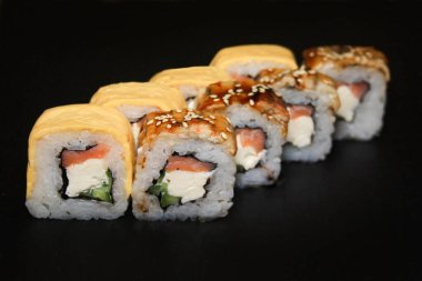 Suşi rulo, yılan balığı ve suşi peynirli ve somonlu siyah arka planda..