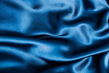 Şatafatlı mavi saten kumaş perdeler yumuşak dokusunu ve zengin rengini vurgulayan bir yüzey boyunca nazikçe uzanır..