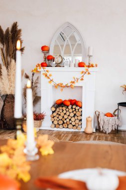 Şık bir oturma odasında balkabağı ve yapraklarla süslenmiş beyaz bir şömine bulunur. Ahşap kütükler mantonun altına istiflenir ve parlak bir uzayda ılık bir sonbahar ortamı yaratır..