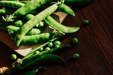Parlak yeşil bezelye kabukları ve küçük bezelyeler taze dokularını ve canlı renklerini gösteren ahşap bir tahtaya konur..