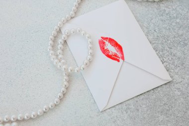 Zarif beyaz bir zarf parlak kırmızı bir öpücükle süslenmiş pürüzsüz gri bir yüzeyde duruyor..