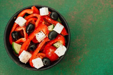 İçinde taze kırmızı biber, salatalık, siyah zeytin ve küp peynir bulunan Yunan salatası. Bu renkli yemek siyah biberle kaplanmış ve siyah bir kasede servis ediliyor..
