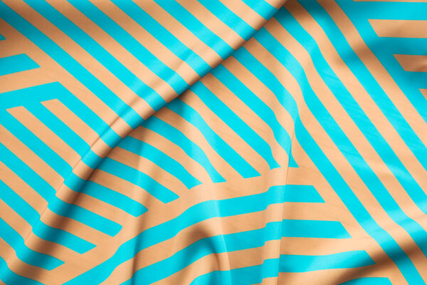 Ткань отображает яркий дизайн с яркими голубыми полосами, установленными на мягком оранжевом фоне. Складки и кривые материала повышают визуальную привлекательность и текстуру.