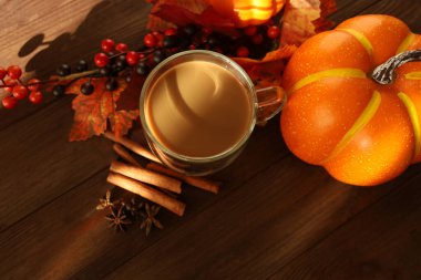 Berrak bir fincan kahve rengarenk sonbahar yapraklarıyla çevrili kırsal ahşap bir masada oturur. Küçük bir balkabağı tarçın çubuğu ve böğürtlen mevsim için sıcak ve davetkar bir atmosfer yaratır..