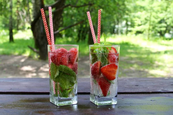 Letnie zimne napoje koktajl truskawkowy ze świeżymi jagodami i mięty w szklance na drewnianym stole w ogrodzie, latem. — Zdjęcie stockowe