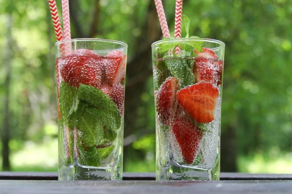 Summer cold drinks Strawberry cocktail with fresh berries and mint in glass on wooden table in garden, summertime.