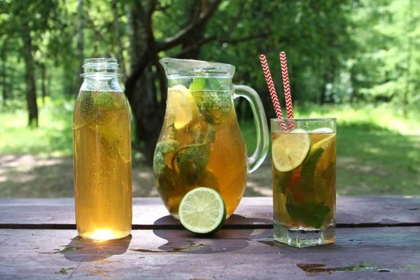 Чай Kombucha забродивший супер еда в стекле, кувшин и бутылка с мятой и лимоном, лайм на деревянном столе, на открытом воздухе . — стоковое фото