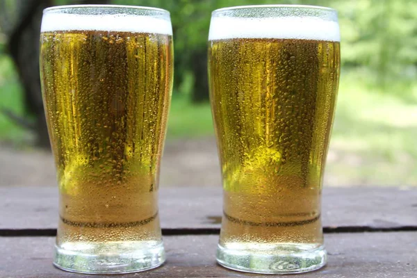 Ahşap masada iki bardak altın soğuk bira, açık havada. Kopyalama alanı ile, yakın.