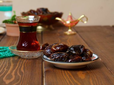 Geleneksel ramazan yemekleri (hurma, çay, su) ve halı sarma arka planı.