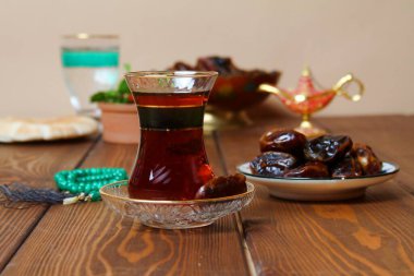 Geleneksel ramazan yemekleri (hurma, çay, su) ve halı sarma arka planı.