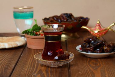 Geleneksel ramazan yemekleri (hurma, çay, su) ve halı sarma arka planı.