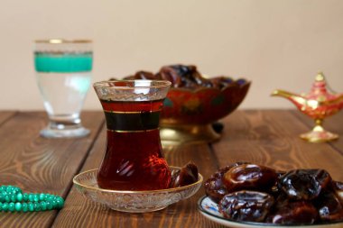 Geleneksel ramazan yemekleri (hurma, çay, su) ve halı sarma arka planı.