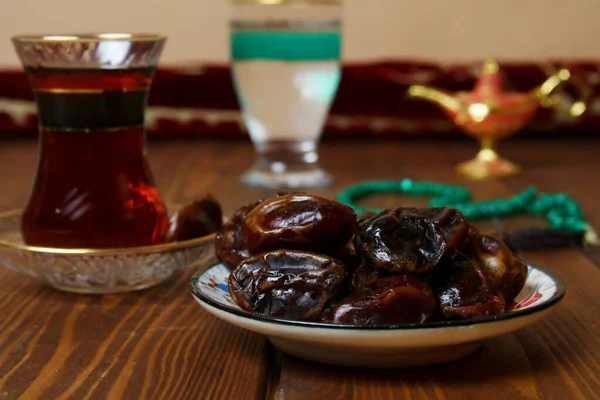 Geleneksel ramazan yemekleri (hurma, çay, su) ve halı sarma arka planı.