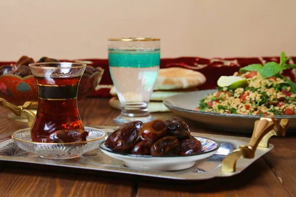 Geleneksel ramazan yemekleri (hurma, çay, su) ve halı sarma arka planı.