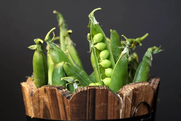 Green pea pod in wooden tub on black background. Close up, macro
