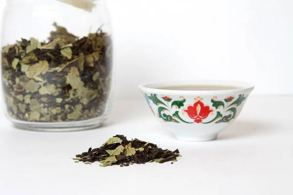 Bitkilerle geleneksel siyah çay ve tatar süsüyle piala, beyaz arka planda cam kavanoz izoza. Yan Görünüm.