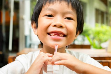 Beyaz t-shirt akıllı bir çocuk ile onun kırık diş gülümsüyor ve cam tüp su içmeyi deneyin.