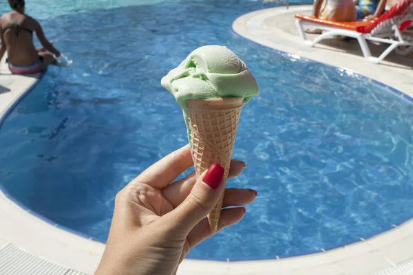 Green ice-cream with waffle on the swimming pool background in hand