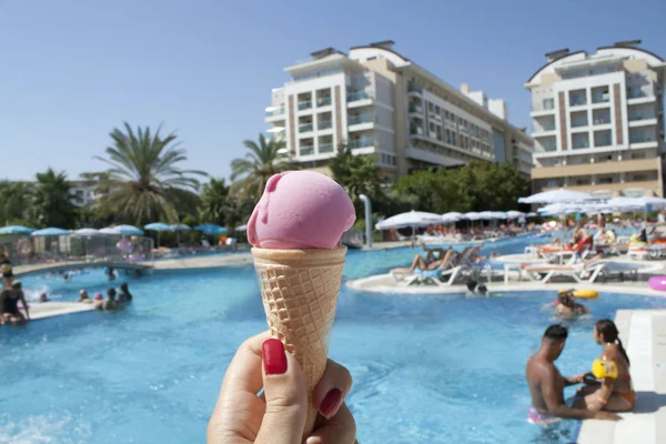 Pink ice-cream with waffle on the swimming pool background in hand