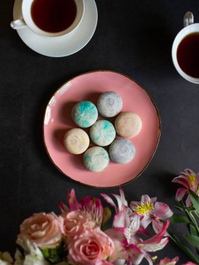 koyu bir masa üzerinde pembe plaka üzerinde çok renkli makarnalar. beyaz bir fincan çay veya kahve. tatlı ile kahvaltı. çiçek buketi