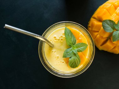 metal saman ile karanlık bir yüzeyde vintage cam bardak mango smoothie / mango lassi üst görünümü. nane yaprakları ve olgun ve sulu mango bir dilim ile