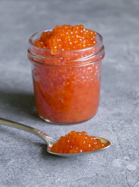 gri beton dokulu yüzey üzerinde cam bir kavanozda kırmızı havyar. gümüş kaşıkta kırmızı havyar