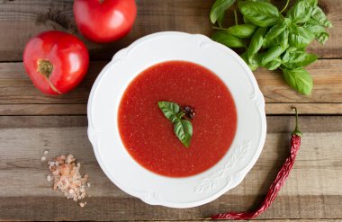 Tahta bir yüzeyde beyaz bir tabakta soğuk soğuk çorba manzarası. Domates, fesleğen, kırmızı biber, Himmalay tuzu.