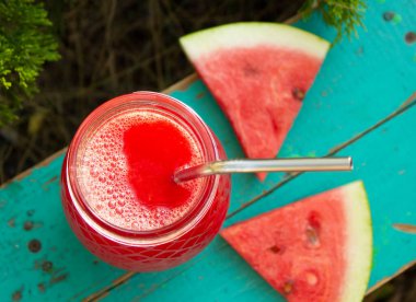 Nefis bir cam kavanozda taze karpuz suyu ve meyve suyu manzarası. İki dilim karpuzla eski bir turkuaz yüzeyde