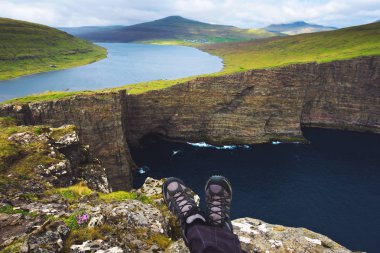 Faroe Adaları'ndaki Sorvagsvatn Gölü üzerindeki bir uçurumun tepesinde oturan yürüyüşçünün bacakları