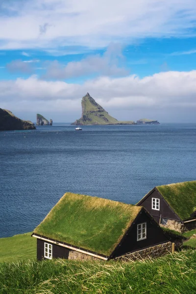 Házak a Feröer-szigetek tengerpartján Drangarnir tengeri verem a háttérben — Stock Fotó