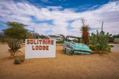 Namibya çölünde bir araba enkazı ile Solitaire Lodge hoş geldiniz işareti