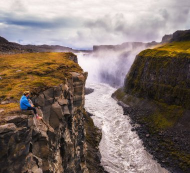 İzlanda 'da Gullfoss şelalesinin kenarında oturan yürüyüşçü.